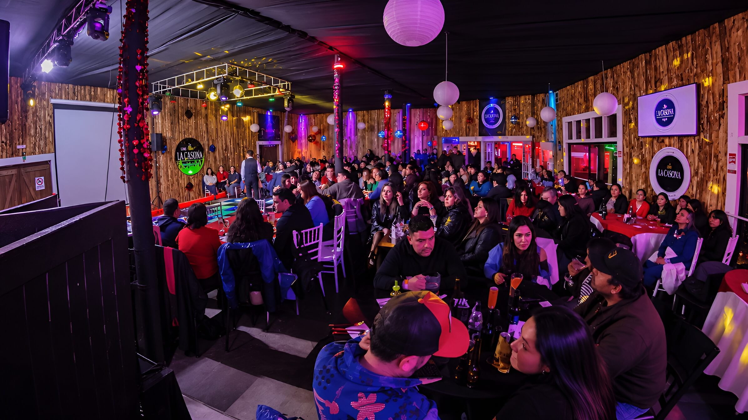 Salón de Club La Casona lleno de público durante un evento en vivo, con pantallas y luces del restobar
